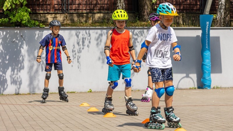 Dzieci uczące się jazdy na rolkach w kaskach i ochraniaczach w ramach
sportowej kolonii oraz letnich półkolonii
